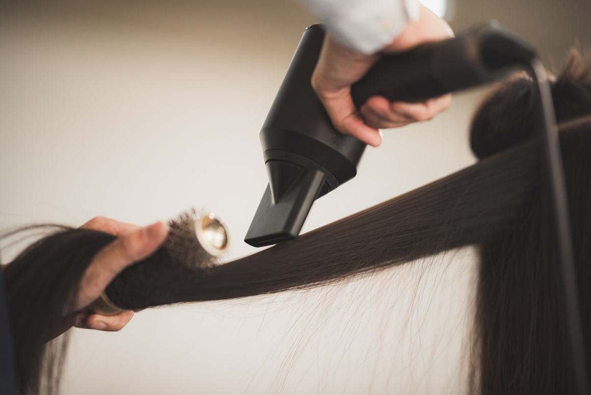 Young hairstylist  drying hair and blowdrying hair of to beautiful long black  hair young woman in beauty salon